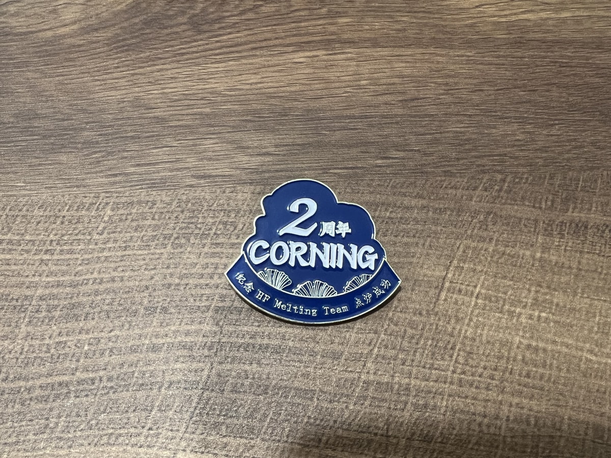 A blue Corning two-year commemorative badge for the HF Melting Team, photographed on a wooden surface.